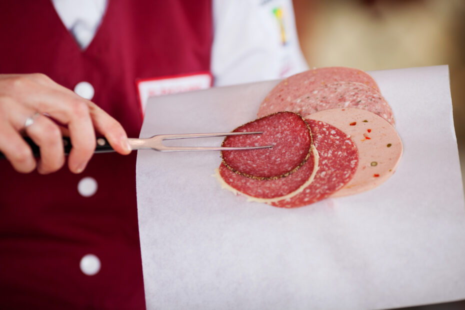 Midsection of female butcher picking up salami with meat fork